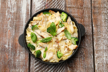 Delicious pasta Alfredo with chicken, cheese, creamy sauce, broccoli and basil on wooden table, top view
