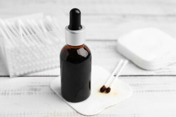 Bottle of iodine with dropper, cotton pads and swabs on white wooden table, closeup
