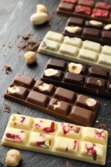 Different tasty chocolate bars with nuts and freeze dried raspberry on black table, closeup