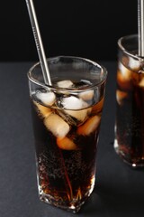 Refreshing cola with ice cubes and drinking straws in glasses on black table, closeup