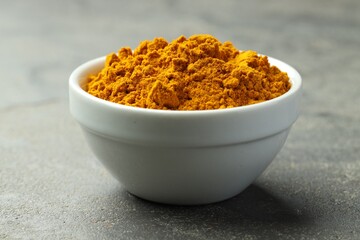 Turmeric powder in bowl on grey table, closeup