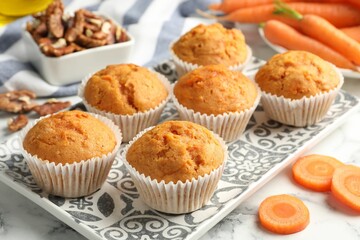 Tasty carrot muffins, fresh vegetables and walnuts on white marble table, closeup