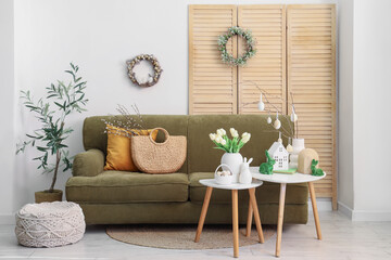 Interior of light living room with sofa, folding screen and Easter wreaths