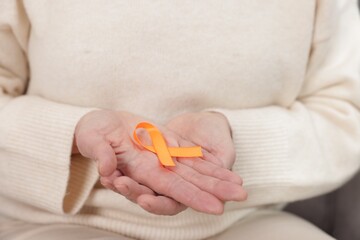 Multiple Sclerosis awareness. Woman with orange ribbon at home, closeup