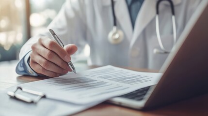 A healthcare professional reviews documents while using a laptop, highlighting the integration of technology in modern medical practices.