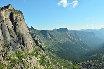 A ridge of high cliffs overlooking a picturesque valley illuminated by the rays of the rising sun on a sunny summer morning.