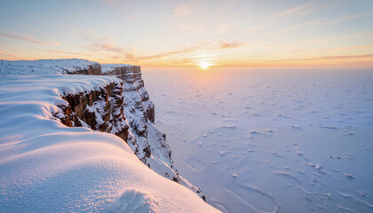 Snow-covered cliff during sunset over frozen ocean