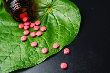 Red herbal capsule pill with herbs and natural green betel leaf background