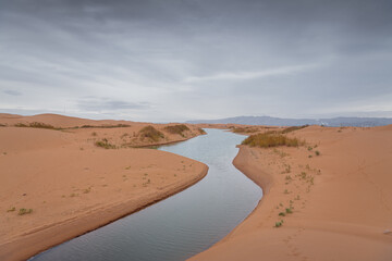 Big dune and the sand texture with the river cutting through at the foreground, Inner Mongolia, China. Background, copy space for text, beige colors, panorama