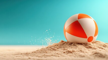 Obraz premium Beach ball resting on a sand dune against a teal background.