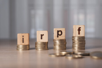 Wooden blocks spelling "IRPF" on stacks of coins, symbolizing income tax