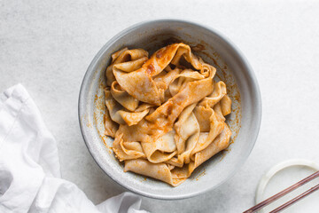 Overhead view of spicy wide noodles in a grey bowl, top view of biangbiang mian in a bowl, spicy belt noodles with green onions and diced pork in a bowl