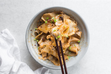 Overhead view of spicy wide noodles in a grey bowl, top view of biangbiang mian in a bowl, spicy belt noodles with green onions and diced pork in a bowl