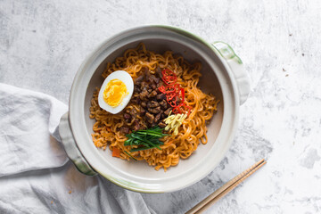 Overhead view of Spicy instant noodles with slices of red chili, ginger and minced pork, spicy ramen noodles in a donabe clay pot