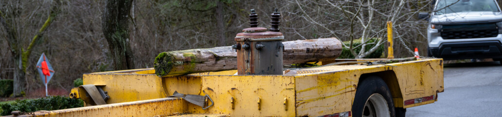 Residential power line maintenance and upgrade, heavy yellow trailer with old removed wood utility pole and rusty transformer, electricity distribution system
