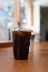 Take home cup with iced black coffee on wood table at coffee shop.