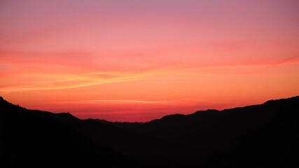 Obraz premium Majestic mountains silhouetted against a vibrant orange and pink sky at sunset, landscape, pink