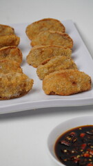 A plate of fried tofu walik served with soy sauce and chili sauce using a separate white plate placed on a white base and background (isolated white).