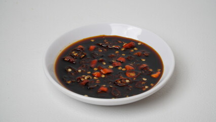 Sweet soy sauce chili sauce with sliced ​​red cayenne pepper served on a white plate placed on a white base and background (isolated white).