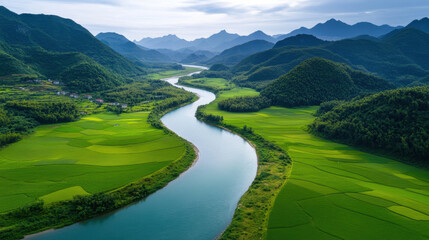 Aerial view of winding river through lush green countryside, surrounded by mountains and fields, creating serene and picturesque landscape