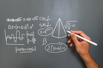 Man's hand writing a mathematical or physics formula on a gray background
