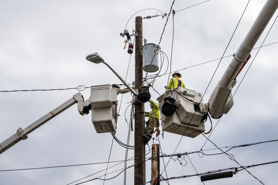 Line crew workman in hydraulic lift bucket, and lineman is climbing gear on wood pole, high up working on utility power lines, residential power line maintenance and upgrade, install new transformer a