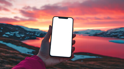 Close-up of a woman holding a cell phone with an empty white screen against a beautiful scarlet sunset over a mountain lake. Phone mockup. The concept of adventure, travel, trekking and exploration