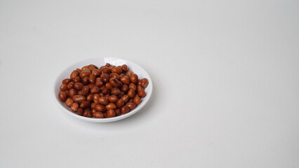 Fried peanuts are served on a white plate and placed on a white background (isolated white).