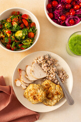 A healthy meal of green buckwheat with chicken breast, zucchini pancakes, fresh and fermented vegetable salads and celery cucumber smoothie
