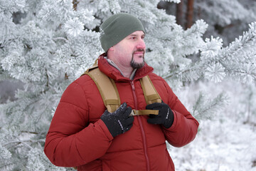 A traveler in a crimson down jacket, equipped with a backpack, stands amidst the snowy woods. A...