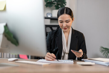 Young committed asian business the data analyst woman counts money in hands sitting  with a desktop computer in the office.
