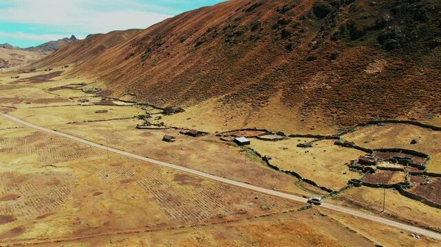 Car drives by high-altitude farming fields and traditional Quechua homes in the indigenous community of Chaullacocha on the Lares trek, Cusco, Peru