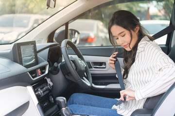 Happy smile brunette asian young woman hand fastens a seat belt sitting in front of car before...