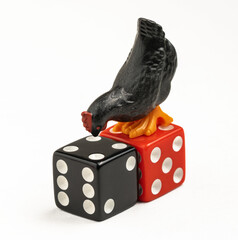 Black toy chicken standing on red and black dice, symbolizing luck, gambling, and unpredictability. © Octavio
