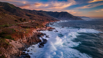 Aerial view of majestic pacific coast seascape along iconic Big Sur Coastline. Where rugged cliffs meet rolling surf in slow motion.  A vibrant sunset.