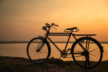 Obraz premium Silhouete of old rusty retro style bicycle during sunrise with golden sky background.
