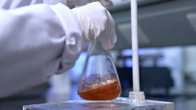 scientist in a lab mixing chemicals in a laboratory. chemist experimenting. science experiment in a beaker flask with colorful chemical liquid in lab with medical lab equipment. chemical concept