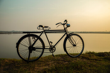Fototapeta premium An old retro bicycle stands in a meadow near a lake at sunrise.
