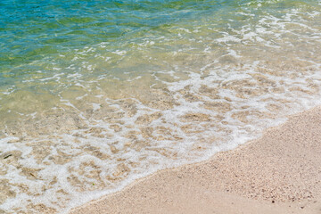 Summer beach sand, blue waves and white foam