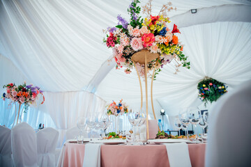 Beautiful flowers decorated on the table with glasses and dishes. Tables set for an event party or wedding reception, luxury elegant table setting dinner in a restaurant In white fancy tent