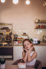 A child girl in a cafe at a table with a cake on the day of the holiday is happy and sweet