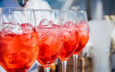 A wine glass filled with ice cubes with red wine, pink vermouth, and a red drink. Cocktail preparation at a party, Iced wine, selective focus. Refreshing cocktail in summer. Beach bar, cold drinks