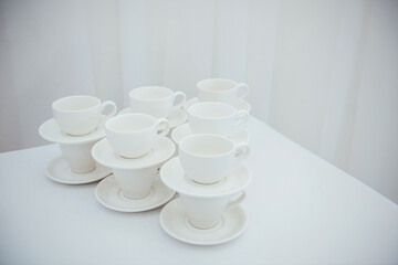 Lots of empty tea or coffee cups on a white table against a white wall, space for text.  Organization of events, catering, catering, beautiful white and gray background