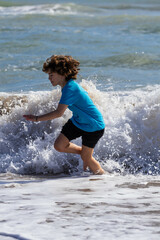 Fototapeta premium Youngster enjoying the ocean. Child runs and plays near the shoreline as waves crash around them on a sunny day at the beach.