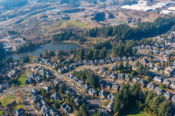 Naklejka premium Aerial drone view of a residential neighborhood in Tualatin, OR, featuring a small lake, tree-lined streets, modern suburban homes, a train track bridge crossing over the water in a peaceful setting