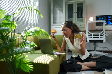 Young businesswoman sitting on the floor in her office, holding a credit card and looking at her...