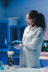 Young female scientist wearing lab coat and protective glasses using laptop, working on innovative...