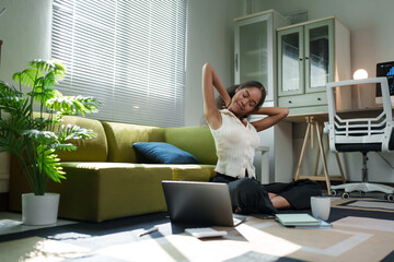 Young manager stretching her neck and arms while sitting on the floor, working remotely from her...