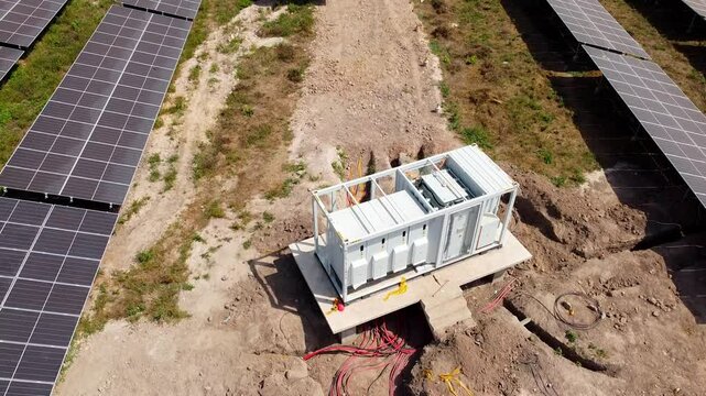 Solar photovoltaic field industrial containerized inverter module with visible DC combiner box cables during installation -aerial low close-up view