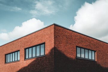 Modern brick building corner under cloudy sky with sunlight creating shadows